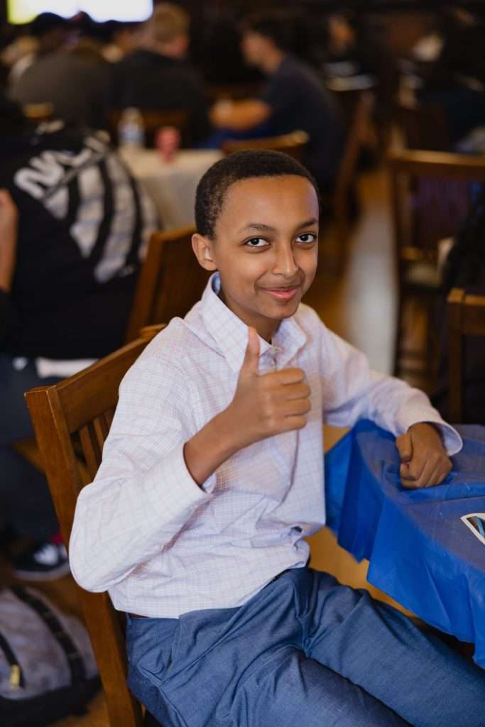 A student seated at a table giving a thumbs-up gesture at the World Affairs Council's Academic WorldQuest competition.
