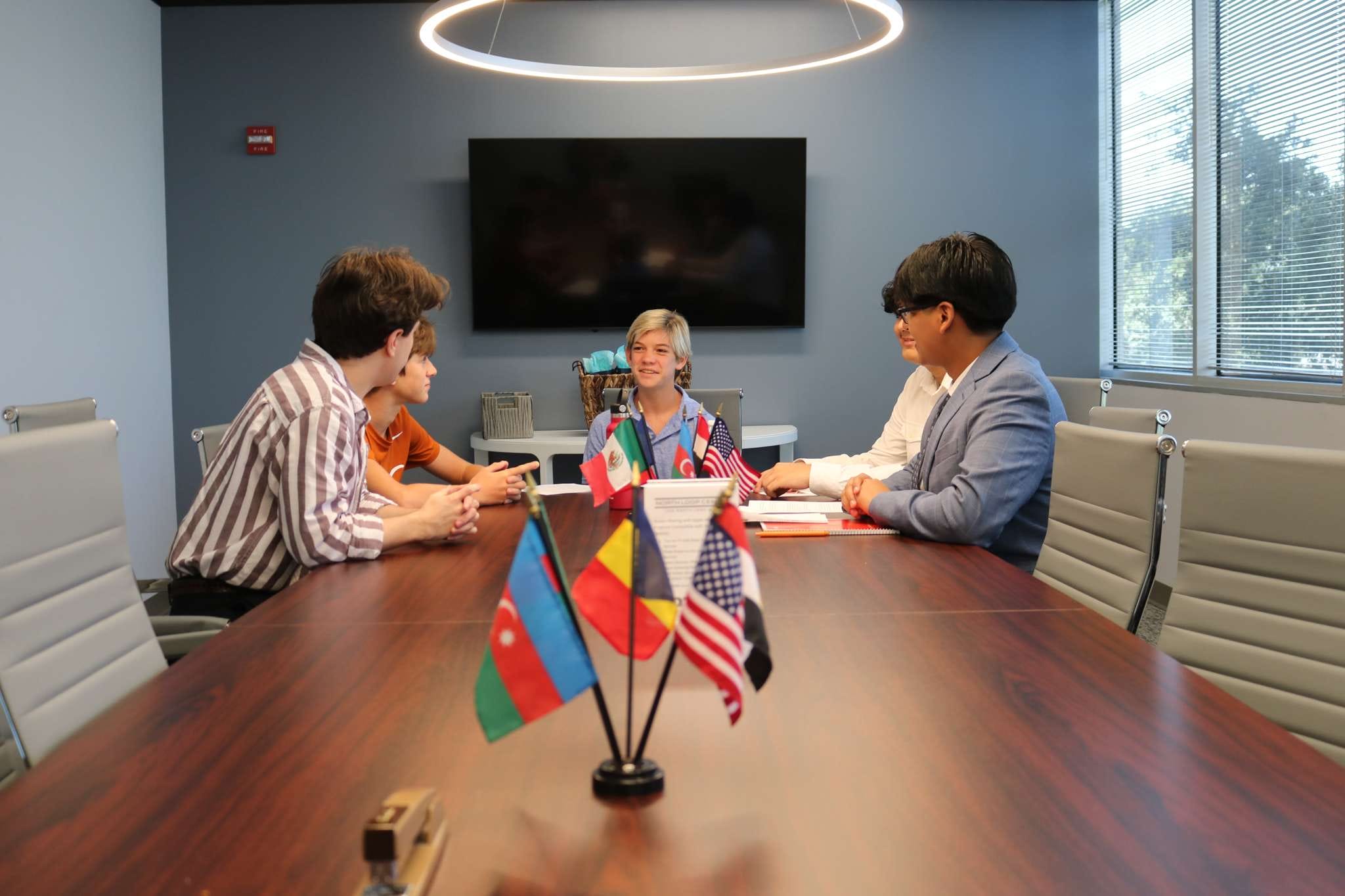 Group of people sitting around a conference table with international flags in the center, having a discussion.