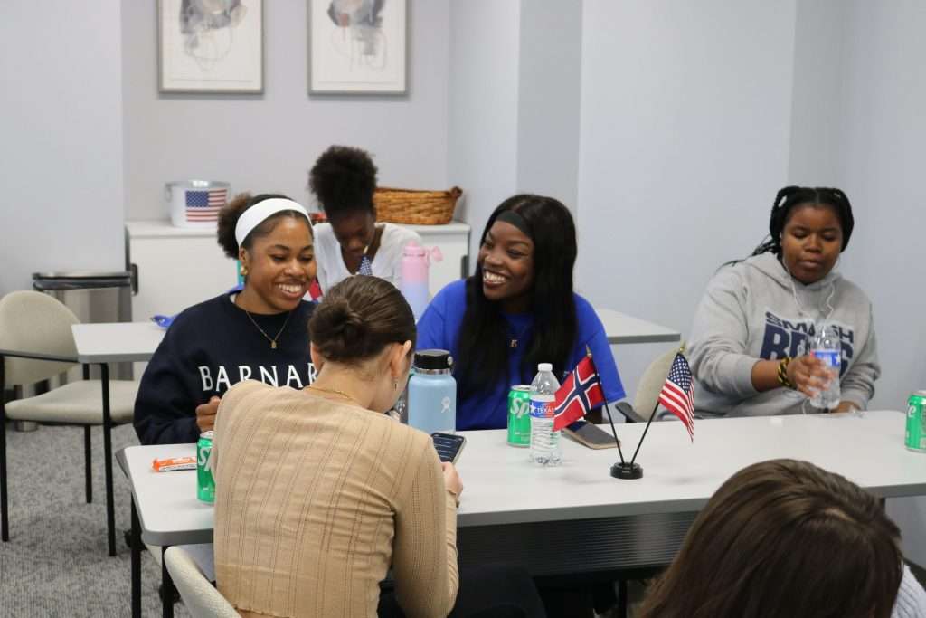 Students laughing and talking at tables, American and Norwegian flags displayed.