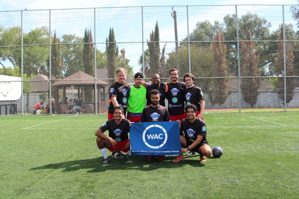 Soccer team posing on field, holding a "WAC" banner, wearing matching black shirts.
