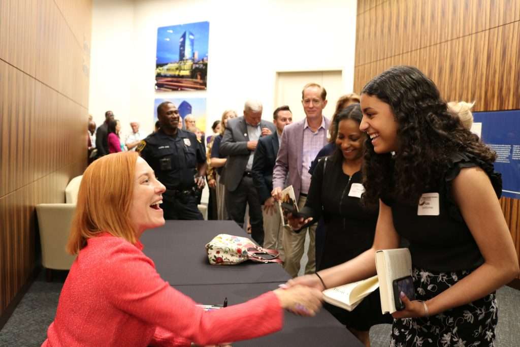 Author in red jacket warmly shaking hands with a fan at signing event.