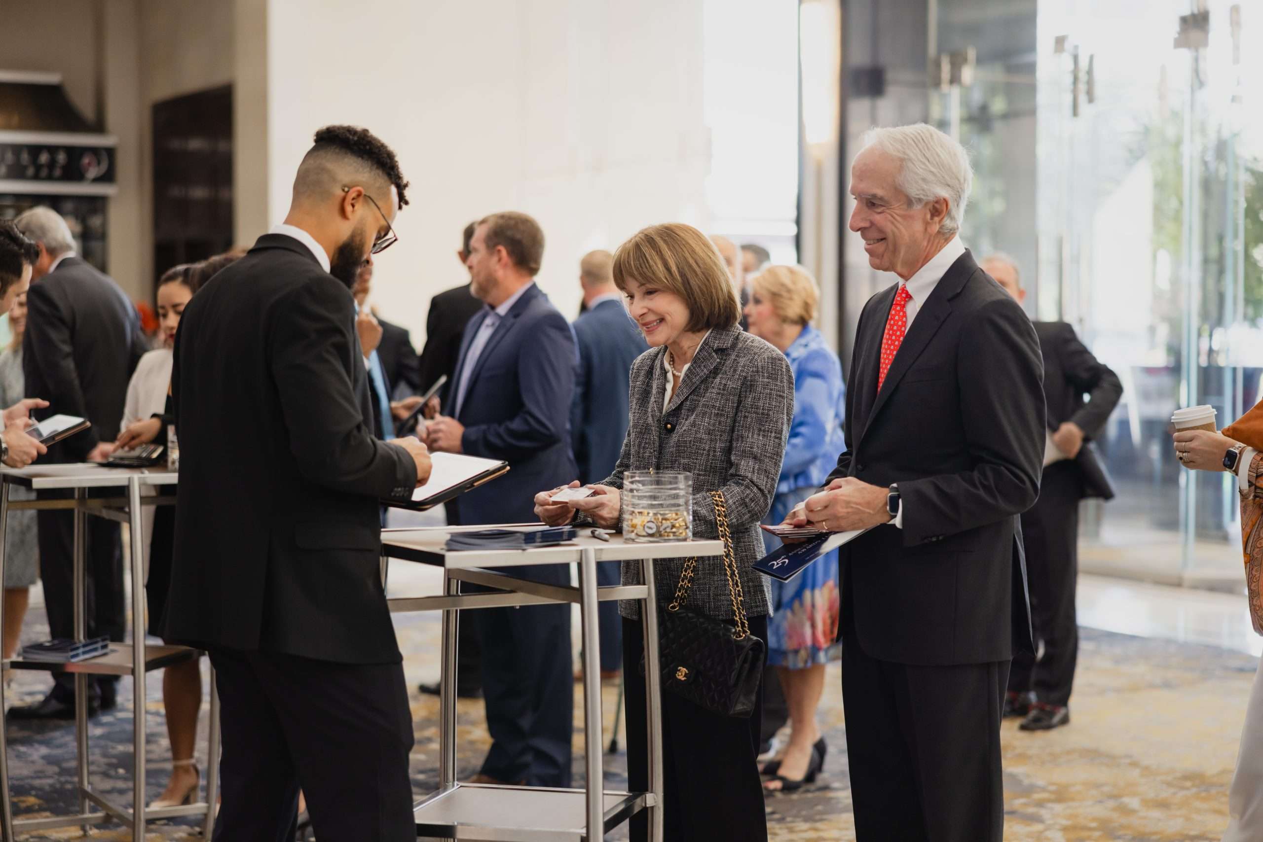Woman and man at a networking event smiling while interacting with a host who is holding a tablet.
