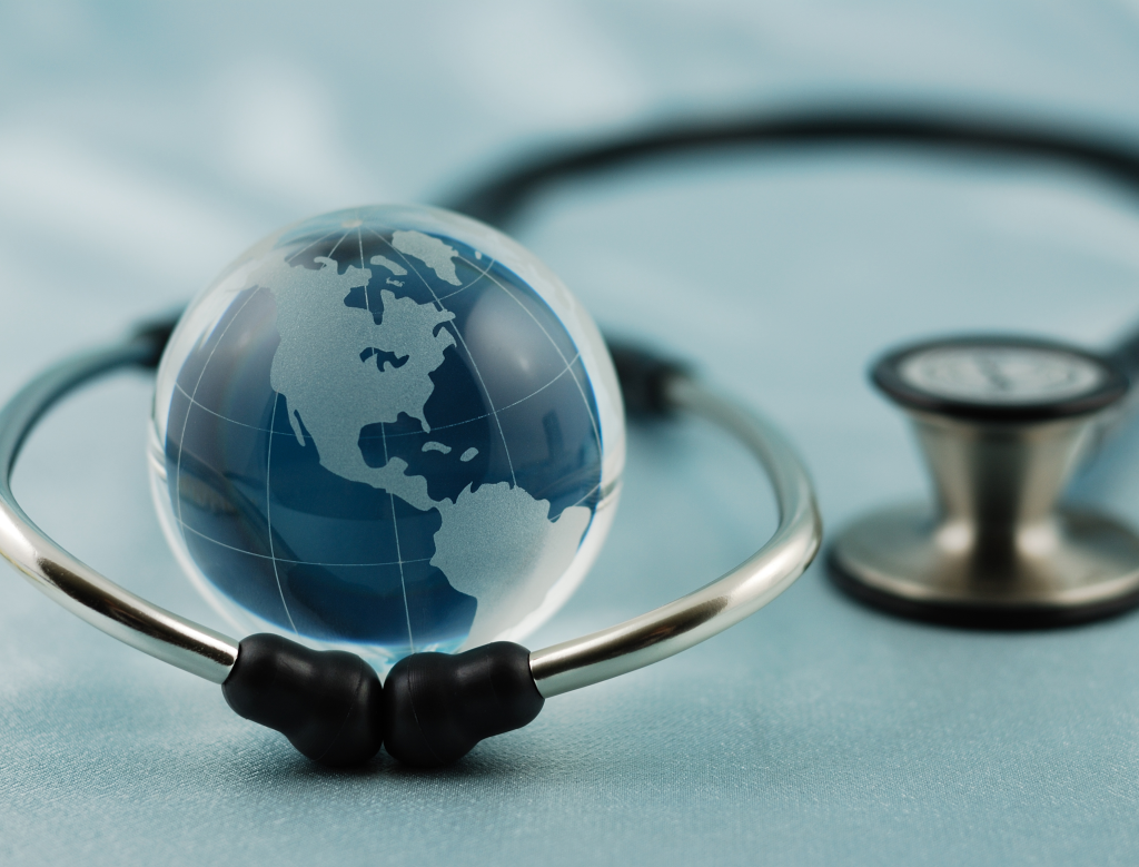 A glass globe with a map of the Americas is encircled by a stethoscope, symbolizing global health care. The background is a soft blue, with the stethoscope’s chest piece resting beside the globe.